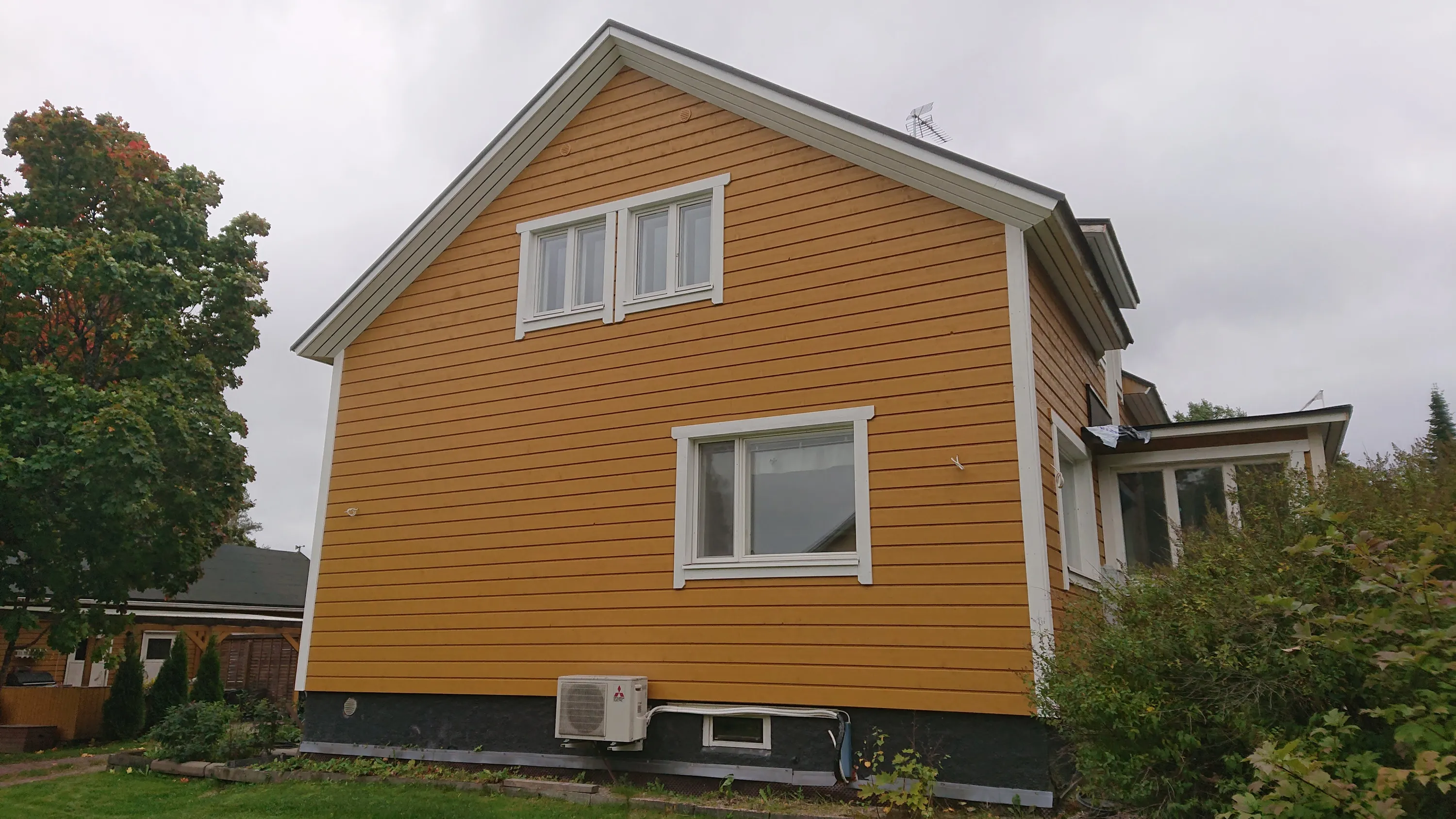 Keltainen puutalo, jossa on valkoiset ikkunat ja seinällä ilmastointilaite.